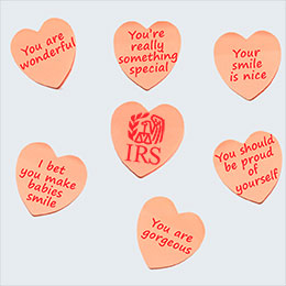 Six pink paper hearts with written messages in red, surrounding pink heart with red IRS logo on light gray background