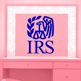 A pink lit up vanity mirror against a pink background with a blue IRS logo in the center of the mirror.
