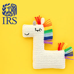 White crochet unicorn with rainbow mane and tail in the foreground. Yellow background. Blue IRS logo. 