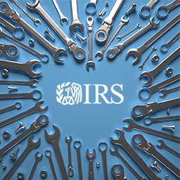 Various sizes of wrenches, nuts and bolts framing the outside edges of a heart shape on a blue background with a white IRS logo in the center.