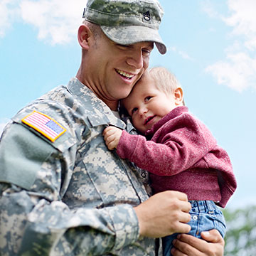 A Soldier holds his child while both have smiles on their faces.